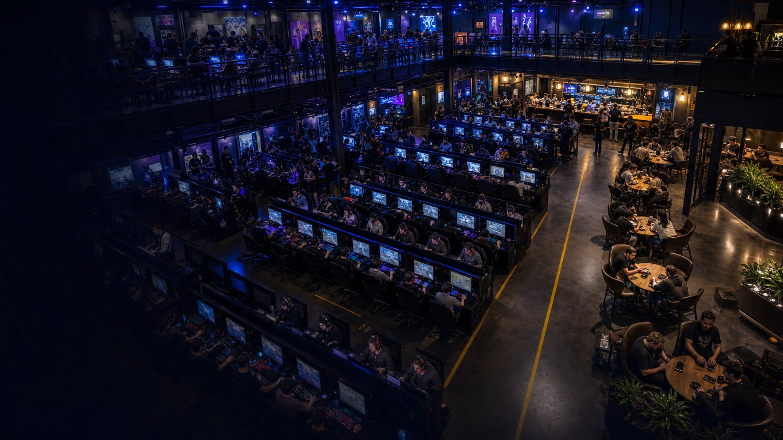 Elevated view across an active multi-level video gaming center with rows of PC stations, a mezzanine, and a social lounge.